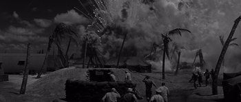 Movie still from “In Harm's Way” (1965), directed by Otto Preminger – A black and white photo of men standing in front of fireworks; Extreme Wide shot, Low angle