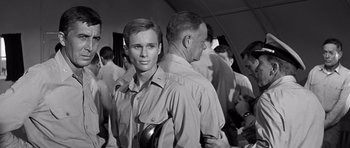 Movie still from “In Harm's Way” (1965), directed by Otto Preminger – A man standing next to another man in front of a group of people; Close Up shot, Over the shoulder angle
