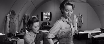 Movie still from “In Harm's Way” (1965), directed by Otto Preminger – A woman is helping another woman put on a shirt; Medium shot, Low angle