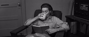 Movie still from “In Harm's Way” (1965), directed by Otto Preminger – A woman sitting in a chair drinking a cup of coffee while reading a book; Medium shot, High angle