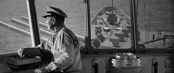 Movie still from “In Harm's Way” (1965), directed by Otto Preminger – An older man in a hat is looking out of a boat window; Medium shot, Over the shoulder angle