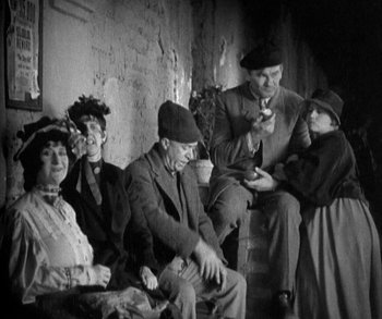 Movie still from “In Old Arizona” (1928), directed by Raoul Walsh – A group of people sitting on steps in an old photo; Medium shot, High angle