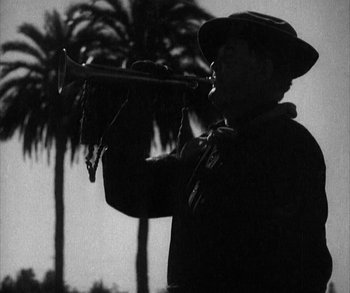 Movie still from “In Old Arizona” (1928), directed by Raoul Walsh – An old man holding a trumpet in front of palm trees; Medium shot, Low angle
