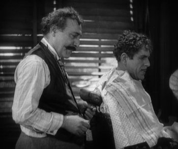 Movie still from “In Old Arizona” (1928), directed by Raoul Walsh – Two men are getting their hair cut at a barber shop; Medium shot, Over the shoulder angle