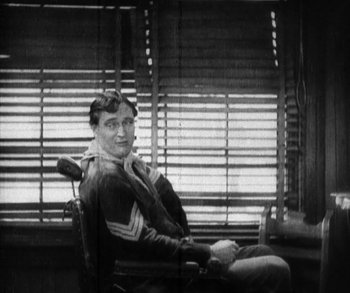 Movie still from “In Old Arizona” (1928), directed by Raoul Walsh – A man sitting in a chair in front of a window; Medium shot, High angle