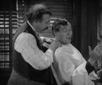 Movie still from “In Old Arizona” (1928), directed by Raoul Walsh – An old photo of a man getting his hair combed by another man; Medium shot, Over the shoulder angle