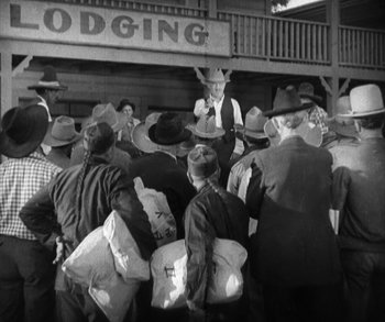 Movie still from “In Old Arizona” (1928), directed by Raoul Walsh – A group of men standing next to each other holding bags; Wide shot, Over the shoulder angle