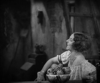 Movie still from “In Old Arizona” (1928), directed by Raoul Walsh – A woman sitting at a table in front of a bowl of fruit; Medium shot, High angle