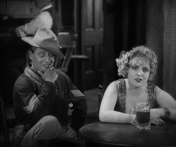 Movie still from “In Old Arizona” (1928), directed by Raoul Walsh – A man and a woman sitting at a table with a glass of beer; Medium shot, Over the shoulder angle
