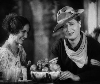 Movie still from “In Old Arizona” (1928), directed by Raoul Walsh – An old photo of a man and a woman sitting at a table with a bowl of fruit; Medium shot, Low angle