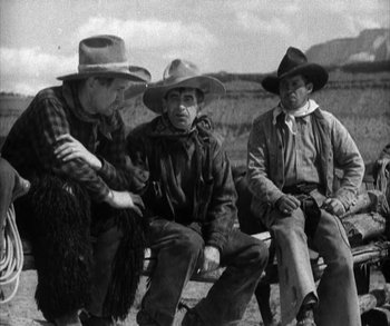 Movie still from “In Old Arizona” (1928), directed by Raoul Walsh – A group of men sitting next to each other on top of a bench; Medium shot, Low angle
