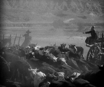 Movie still from “In Old Arizona” (1928), directed by Raoul Walsh – A man riding a bike through a herd of cattle; Wide shot, High angle