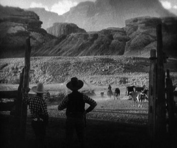 Movie still from “In Old Arizona” (1928), directed by Raoul Walsh – Two men in cowboy hats looking out at cows; Extreme Wide shot, High angle