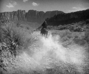 Movie still from “In Old Arizona” (1928), directed by Raoul Walsh – A man riding a horse down a dirt road; Extreme Wide shot, High angle