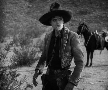 Movie still from “In Old Arizona” (1928), directed by Raoul Walsh – A man wearing a cowboy hat and a cowboy outfit; Medium shot, Low angle