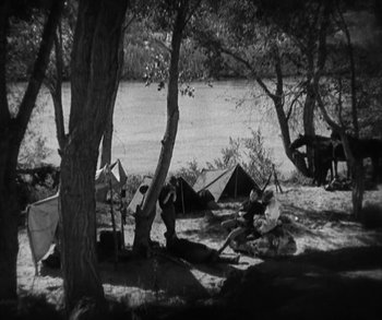 Movie still from “In Old Arizona” (1928), directed by Raoul Walsh – A black and white photo of a group of people camping; Extreme Wide shot, High angle