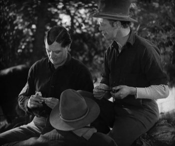 Movie still from “In Old Arizona” (1928), directed by Raoul Walsh – Three men sitting on a bench looking at their cell phones; Medium shot, High angle