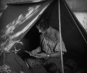Movie still from “In Old Arizona” (1928), directed by Raoul Walsh – A woman sitting under a tent looking at a book; Medium shot, High angle