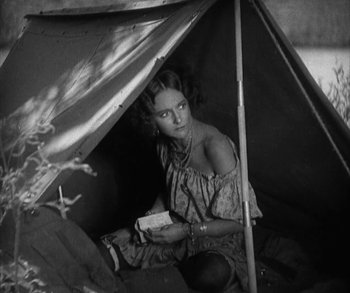 Movie still from “In Old Arizona” (1928), directed by Raoul Walsh – A woman sitting inside of a tent holding a book; Medium shot, High angle