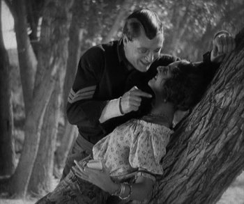 Movie still from “In Old Arizona” (1928), directed by Raoul Walsh – A man and a woman are playing around a tree in the woods; Medium shot, Low angle