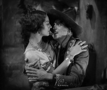 Movie still from “In Old Arizona” (1928), directed by Raoul Walsh – A man and a woman embracing each other in a black and white photo; Medium shot, Low angle