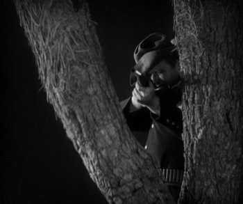 Movie still from “In Old Arizona” (1928), directed by Raoul Walsh – A person in a tree wearing sunglasses and a helmet; Medium shot, Low angle