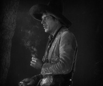 Movie still from “In Old Arizona” (1928), directed by Raoul Walsh – A man wearing a cowboy hat smoking a cigarette; Medium shot, Low angle