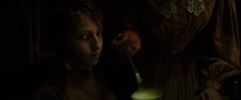 Movie still from “In Secret” (2013), directed by Charlie Stratton – A young boy is looking at the camera while a woman watches; Close Up shot, High angle