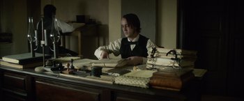Movie still from “In Secret” (2013), directed by Charlie Stratton – A man sitting at a table with papers on it; Medium shot, High angle