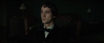 Movie still from “In Secret” (2013), directed by Charlie Stratton – A man in a black suit and a black bow tie; Close Up shot, Over the shoulder angle