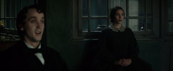 Movie still from “In Secret” (2013), directed by Charlie Stratton – A woman sitting in front of a window in a dark room; Medium shot, Over the shoulder angle