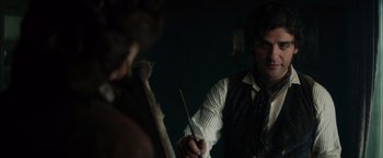 Movie still from “In Secret” (2013), directed by Charlie Stratton – A man holding a wooden stick in his hand while another man looks on; Medium shot, Over the shoulder angle