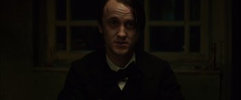 Movie still from “In Secret” (2013), directed by Charlie Stratton – A man with long hair wearing a suit and bow tie; Close Up shot, Low angle