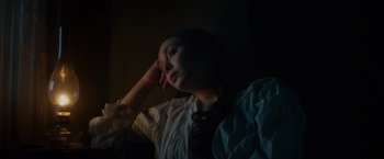 Movie still from “In Secret” (2013), directed by Charlie Stratton – A woman sitting in a dark room with her head resting on her hand; Close Up shot, High angle