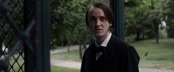 Movie still from “In Secret” (2013), directed by Charlie Stratton – A man with long hair wearing a suit and bow tie; Close Up shot, Over the shoulder angle