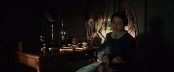 Movie still from “In Secret” (2013), directed by Charlie Stratton – A woman sitting in front of a table with a man sitting on top of it; Medium shot, Over the shoulder angle