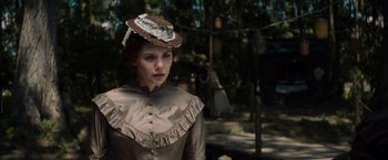 Movie still from “In Secret” (2013), directed by Charlie Stratton – A woman in a brown dress and a brown hat; Close Up shot, Over the shoulder angle