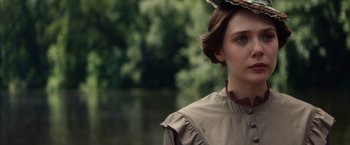 Movie still from “In Secret” (2013), directed by Charlie Stratton – A young woman in a brown dress and a hat; Close Up shot, Over the shoulder angle