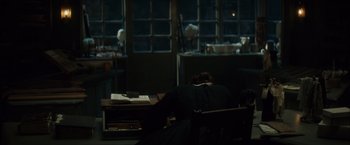 Movie still from “In Secret” (2013), directed by Charlie Stratton – A person sitting at a desk in a dark room; Wide shot, High angle