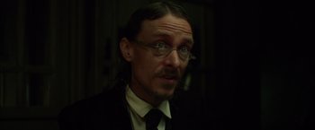 Movie still from “In Secret” (2013), directed by Charlie Stratton – A person wearing a suit and glasses; Close Up shot, Over the shoulder angle