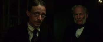 Movie still from “In Secret” (2013), directed by Charlie Stratton – A man in a suit and tie with glasses; Close Up shot, Over the shoulder angle