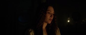 Movie still from “In Secret” (2013), directed by Charlie Stratton – A woman with long curly hair is standing in the dark; Close Up shot, Over the shoulder angle