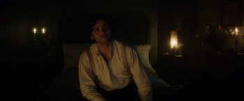 Movie still from “In Secret” (2013), directed by Charlie Stratton – A man sitting on a bed in a dark room; Medium shot, Over the shoulder angle