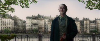 Movie still from “In Secret” (2013), directed by Charlie Stratton – A man standing in front of a building with buildings in the background; Medium shot, Over the shoulder angle