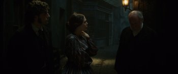 Movie still from “In Secret” (2013), directed by Charlie Stratton – A woman in a dress standing next to a building; Medium shot, Over the shoulder angle