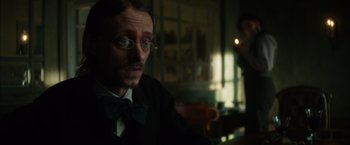 Movie still from “In Secret” (2013), directed by Charlie Stratton – A man in a suit and bow tie looking to his left; Close Up shot, Over the shoulder angle