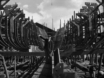 Movie still from “In Which We Serve” (1942), directed by Noël Coward – A man standing in front of a bunch of boats; Wide shot, Low angle