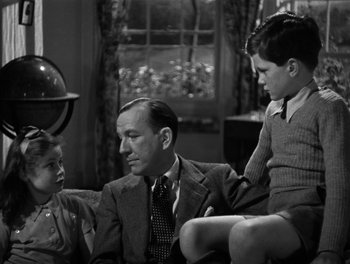 Movie still from “In Which We Serve” (1942), directed by Noël Coward – An older man sitting on a couch with two young boys; Medium shot, High angle