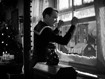 Movie still from “In Which We Serve” (1942), directed by Noël Coward – A man standing in front of a window with his hands in the air; Medium shot, Low angle