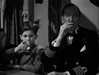 Movie still from “In Which We Serve” (1942), directed by Noël Coward – A man and a boy are sitting at a table drinking wine; Medium shot, Over the shoulder angle